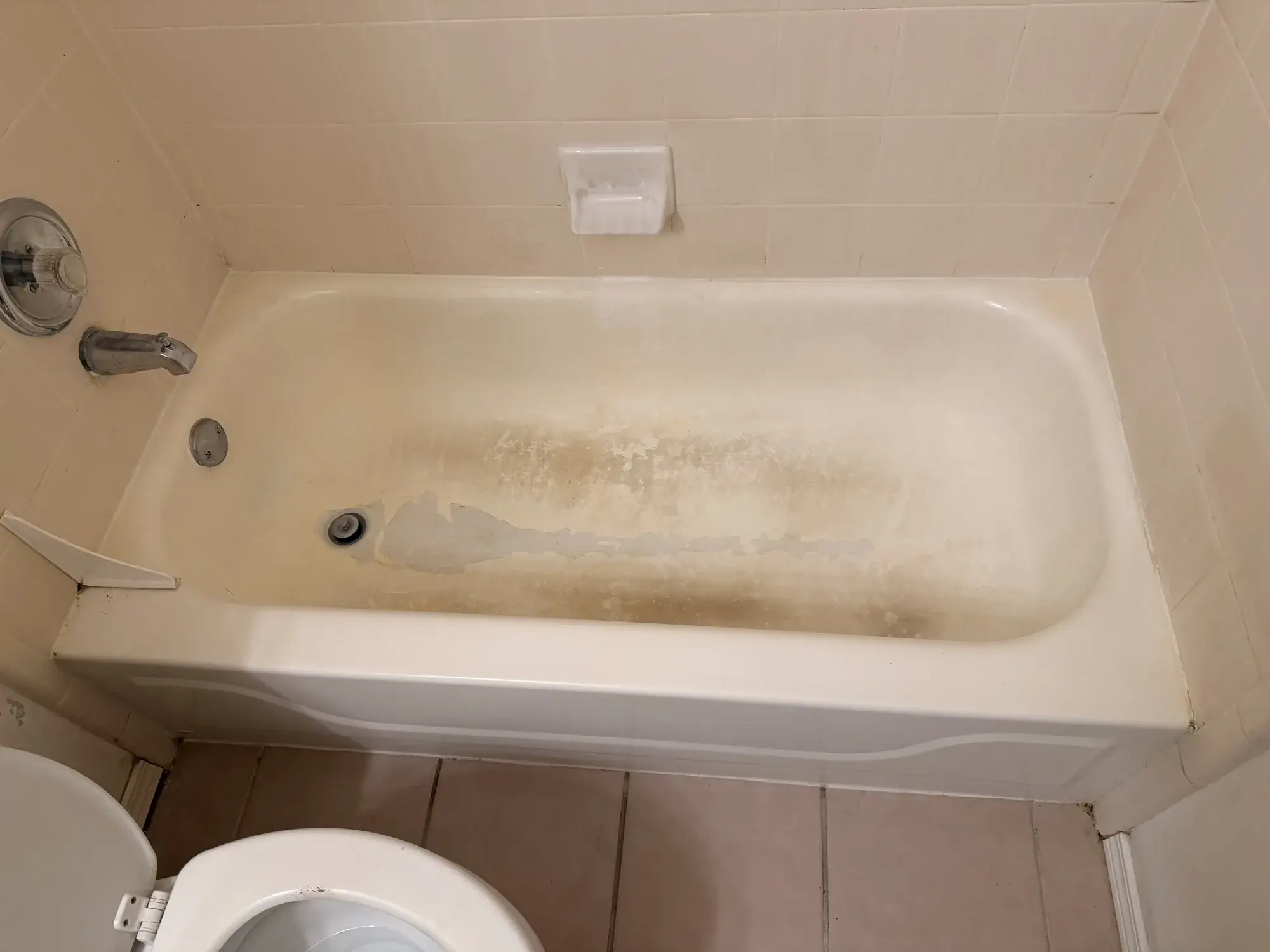 Bathtub before refinishing next to beige tile